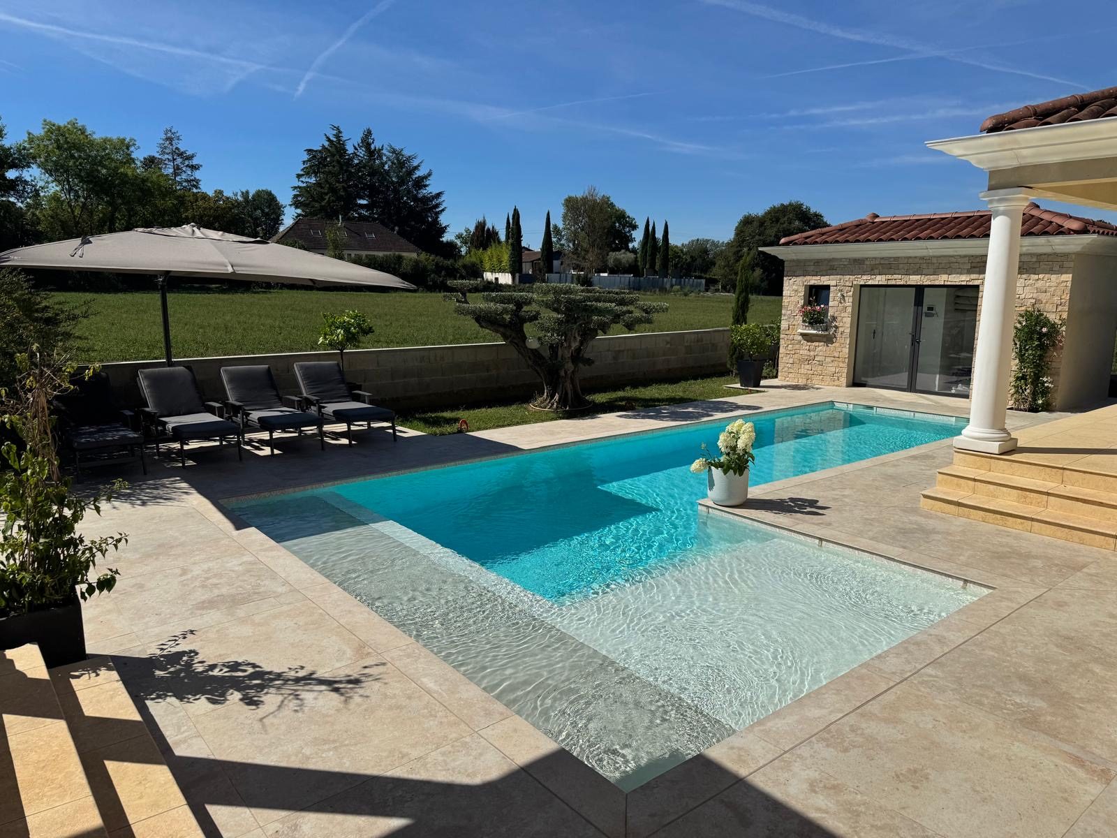 Piscine construite par Les Bassins de Jules, plages en travertin et pool house à colonnes